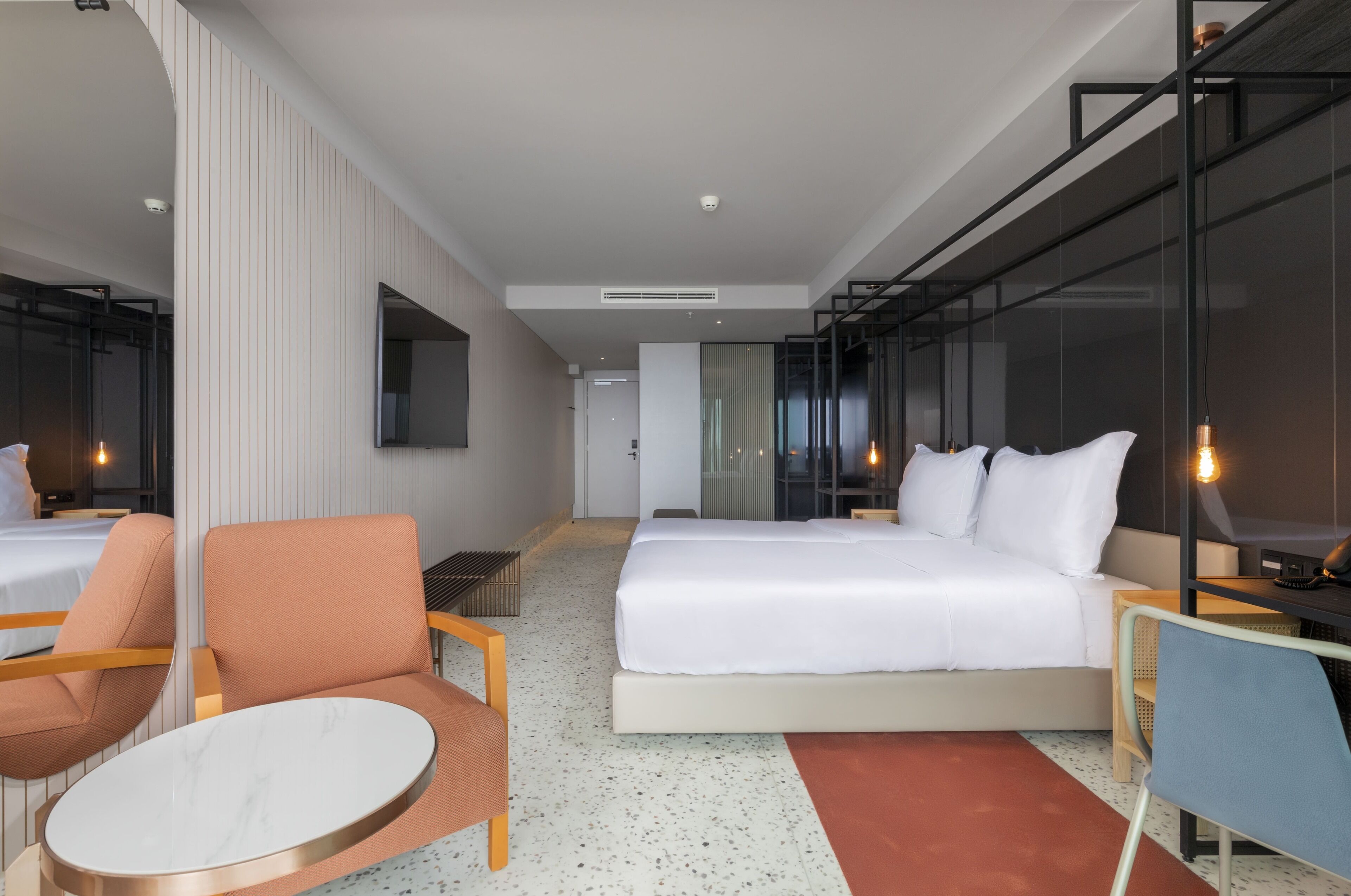 A modern hotel room with a large bed, a seating area with a round table, and a large window.