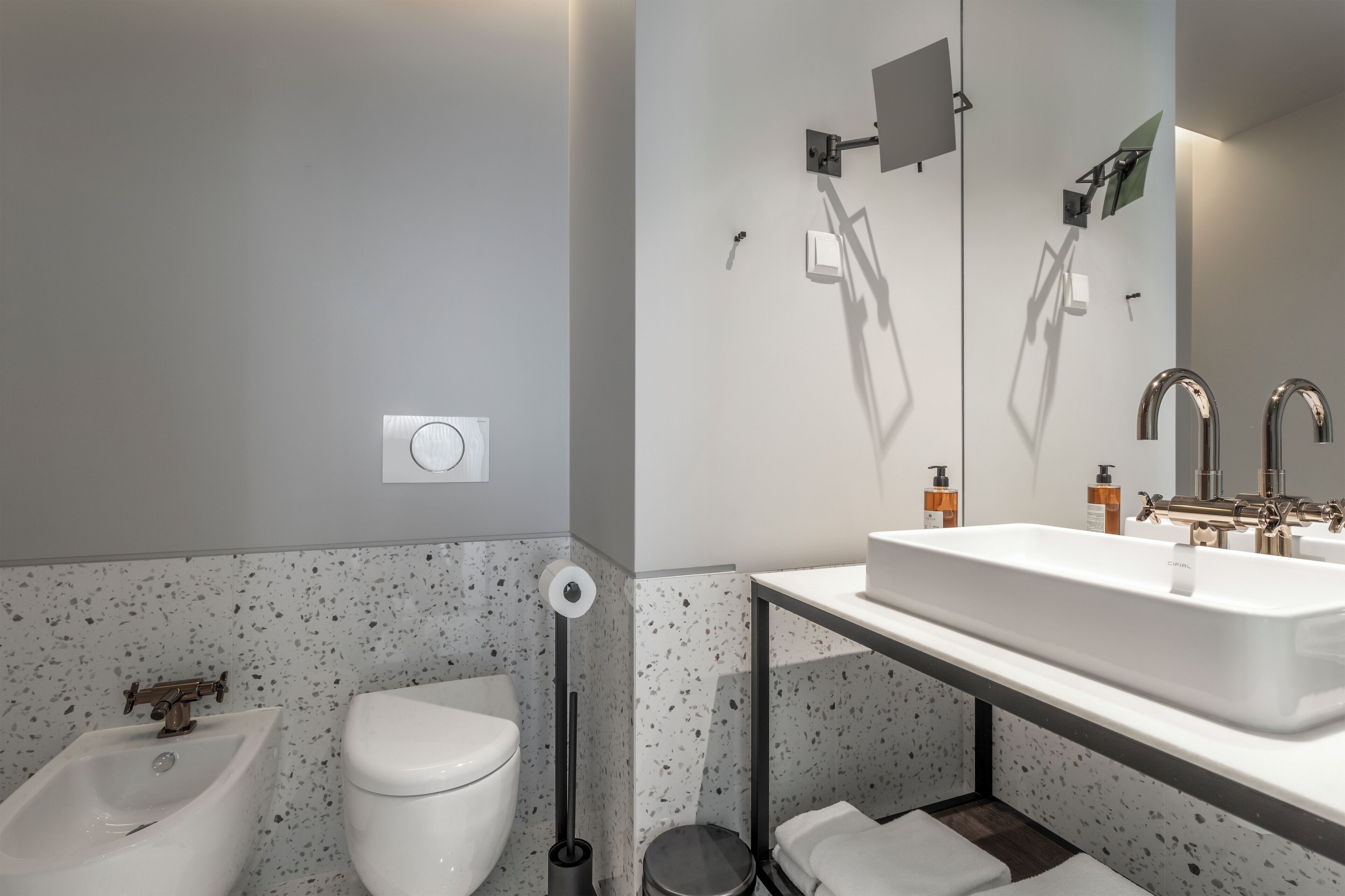 A modern bathroom with a white sink, a bidet, a toilet, and a mirror.