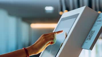 A hand interacting with a digital kiosk, likely for hotel check-in or information.
