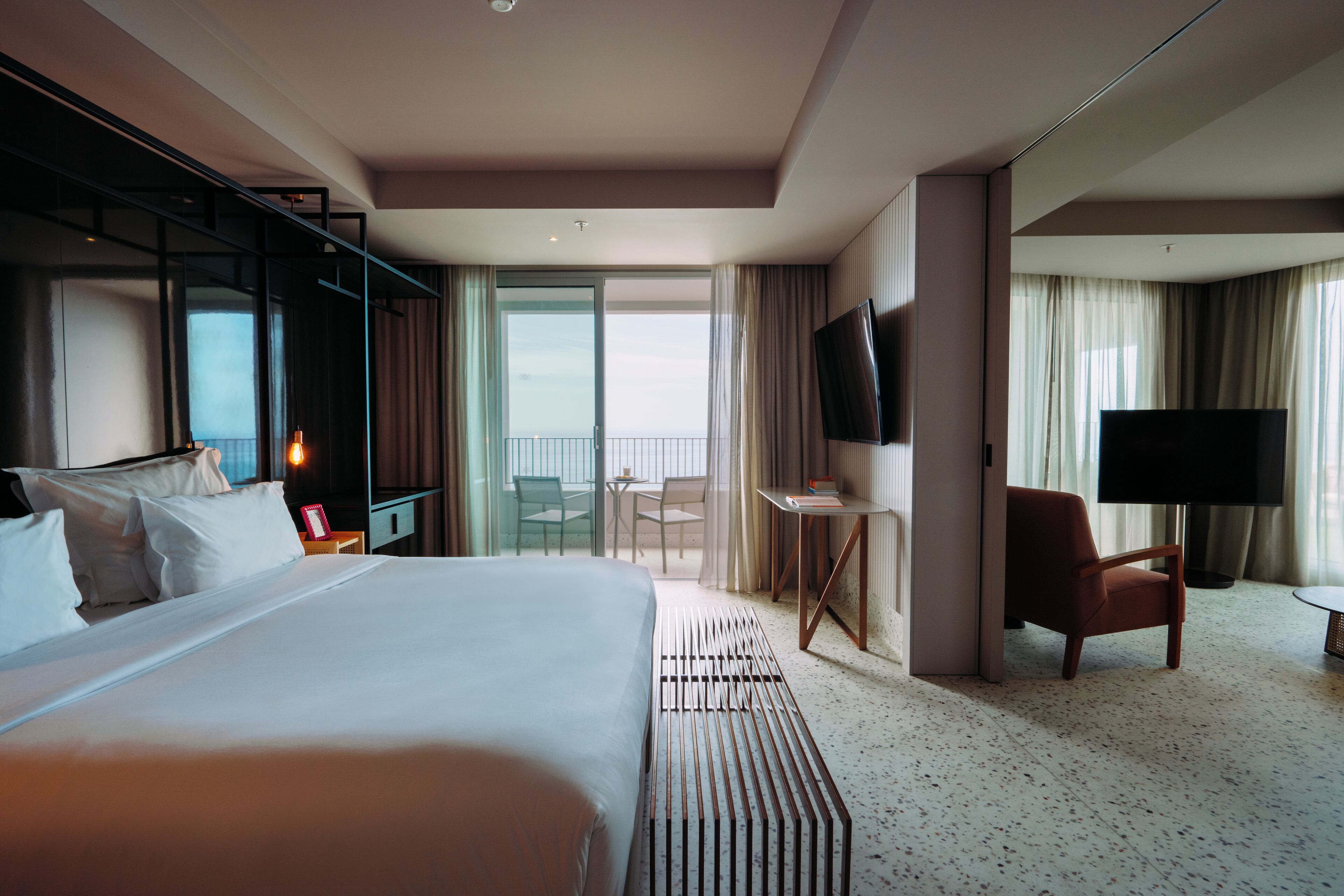 Ein Hotelzimmer mit einem großen Bett, einem Schreibtisch, einem Sessel, einem Fernseher und einem Balkon mit Blick.