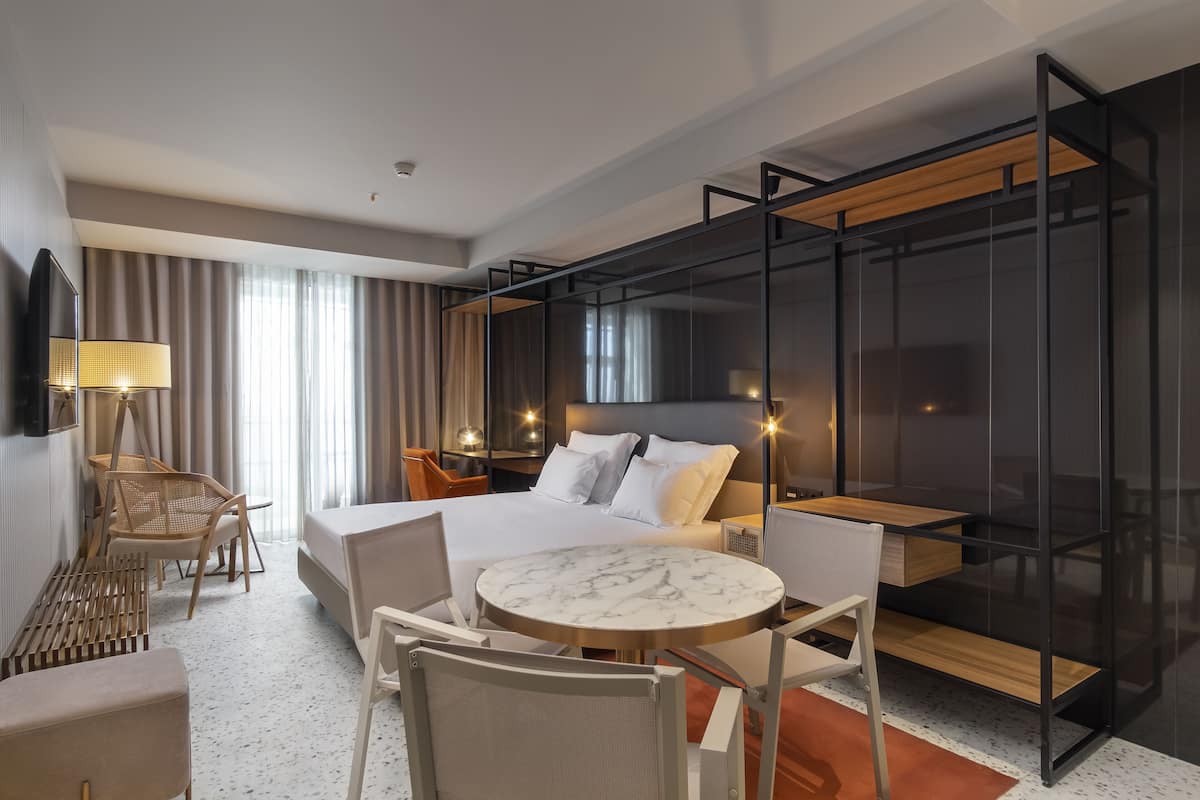 Una habitación de hotel moderna con una cama grande, una mesa redonda de mármol y un separador de vidrio.