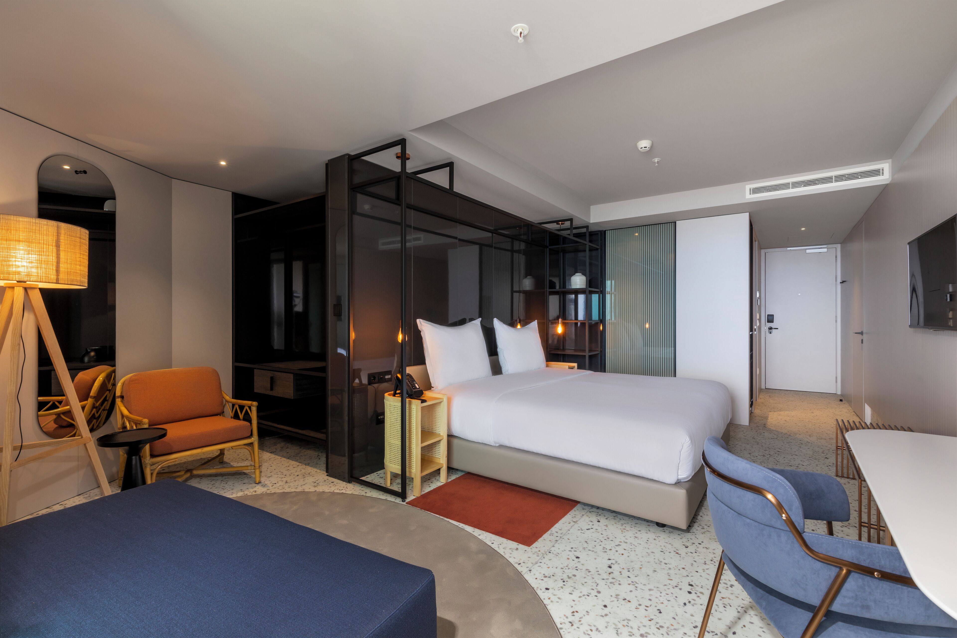 A modern hotel room with a large bed, a desk, a chair, and a sofa.