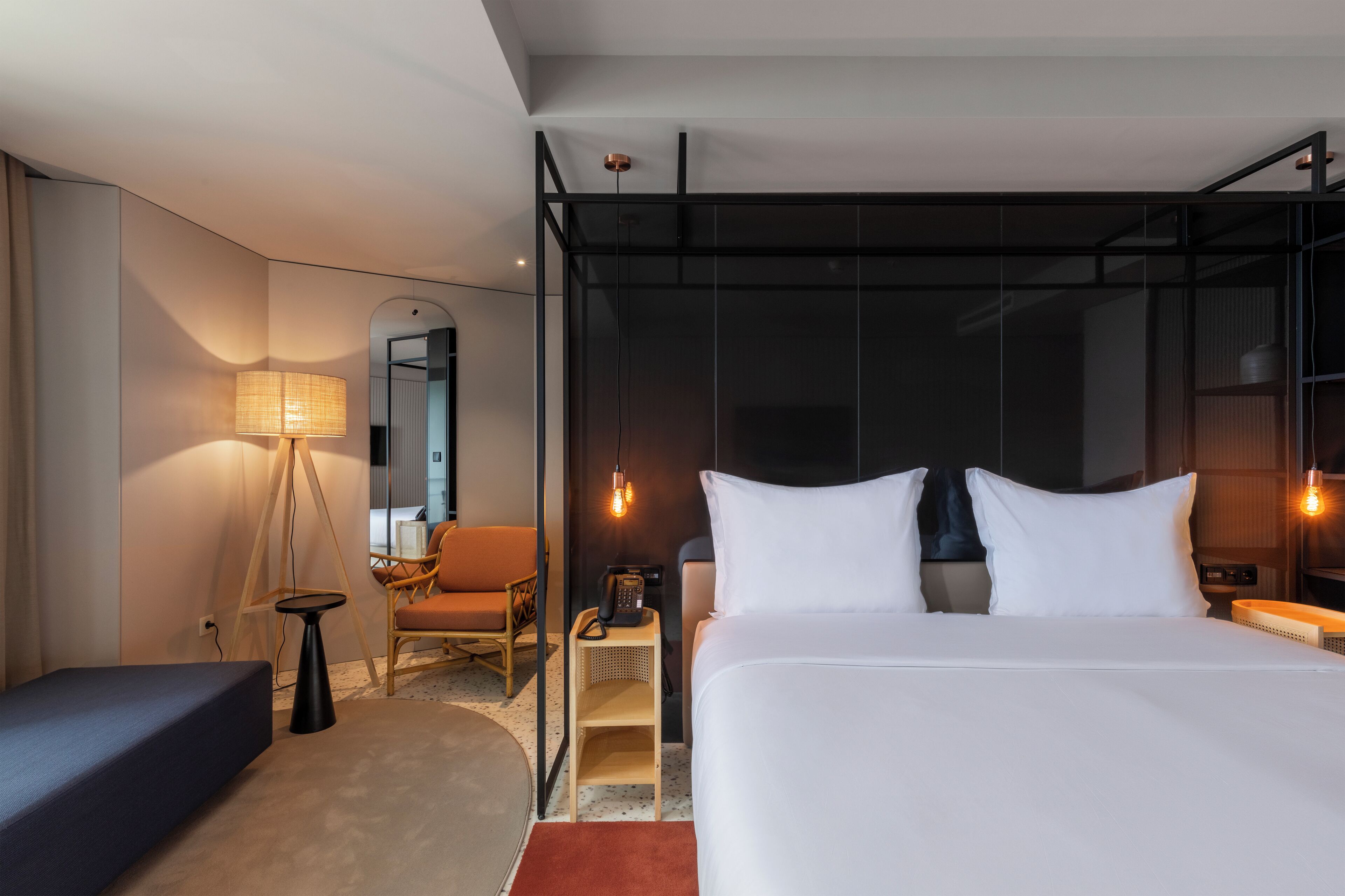 A modern hotel room with a large bed, a desk, a chair, a lamp, and a mirror.