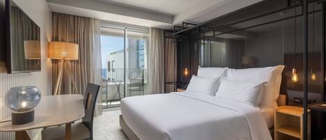 A modern hotel room with a large bed, a desk, and a balcony with a view.