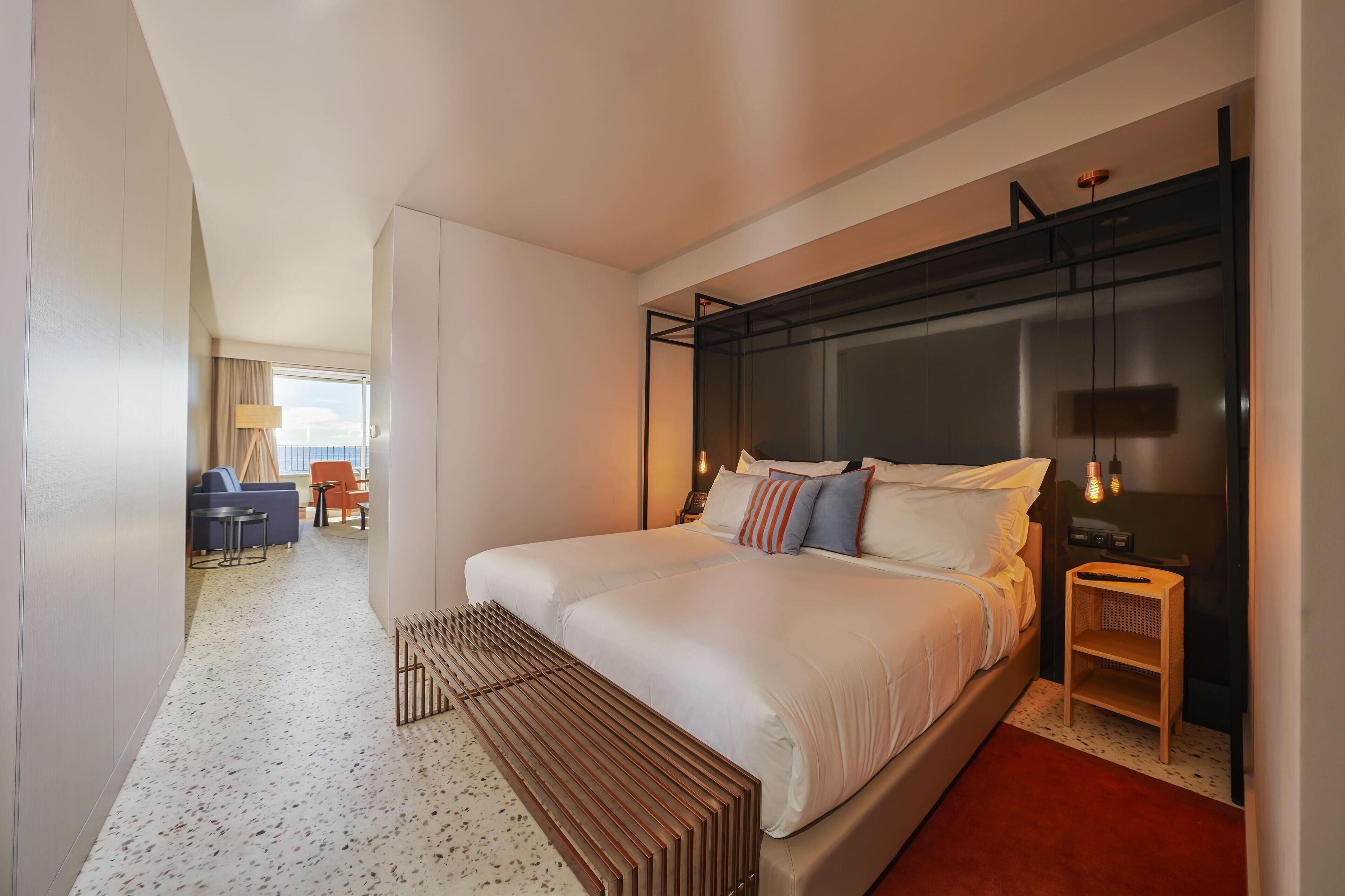 Une chambre d’hôtel moderne avec un grand lit, une table de chevet, une lampe et une vue sur le balcon.