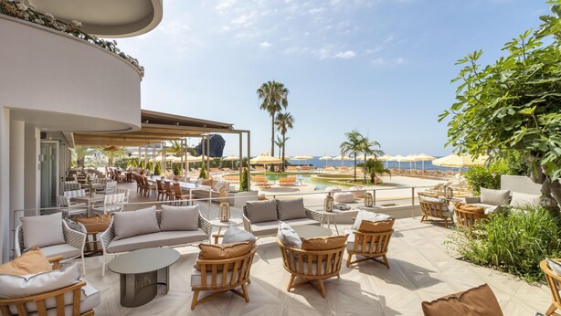Un salón en la azotea con asientos exteriores, una piscina y vista al océano.