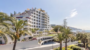 Un hotel de varios pisos con balcones, palmeras y vista al mar.