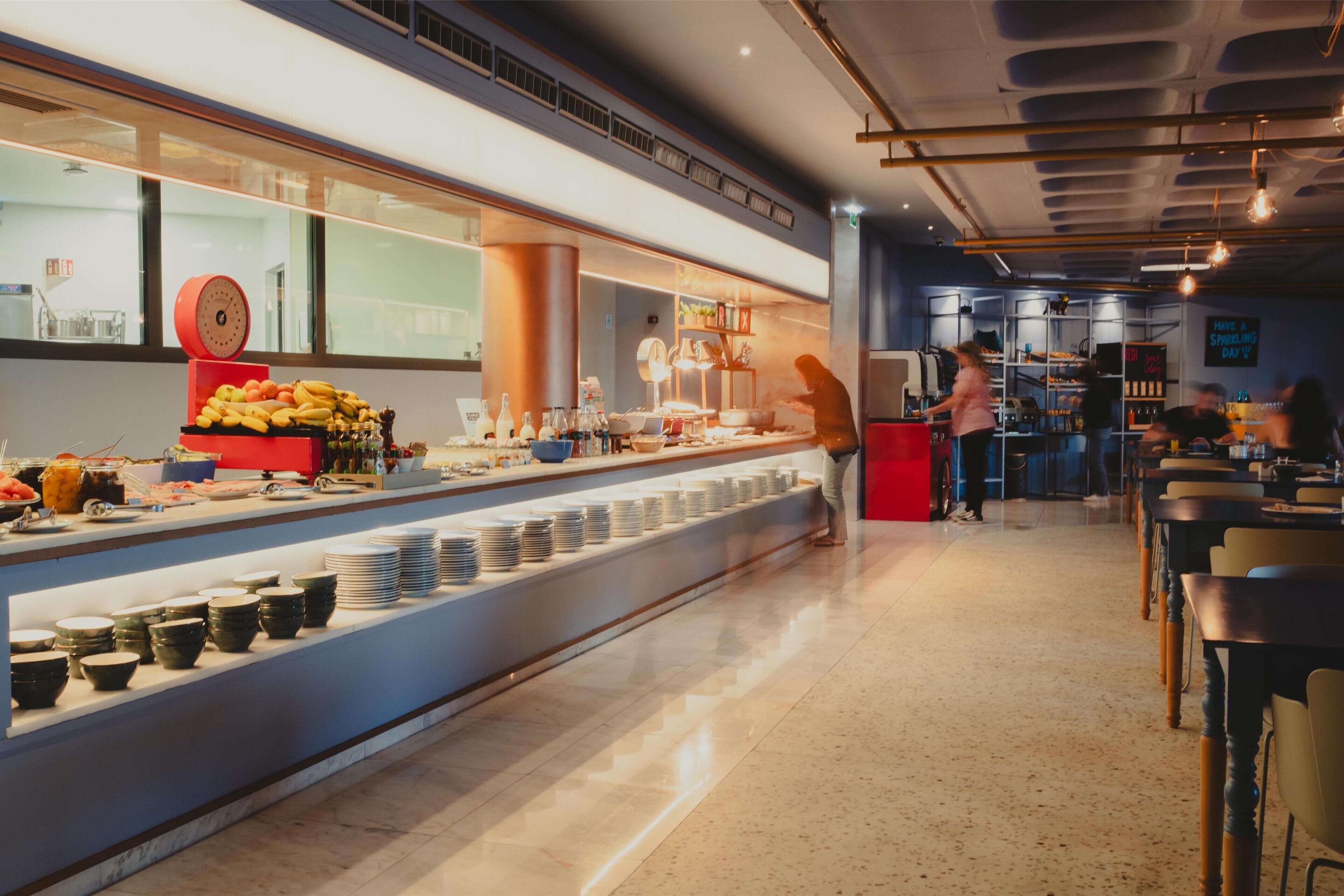 Un espace buffet proposant une variété de plats et de boissons, une balance pour peser les aliments, ainsi qu’un comptoir avec des assiettes et des bols.