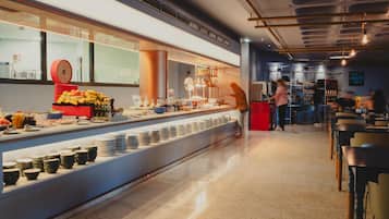 Un espace buffet proposant une variété de plats et de boissons, une balance pour peser les aliments, ainsi qu’un comptoir avec des assiettes et des bols.