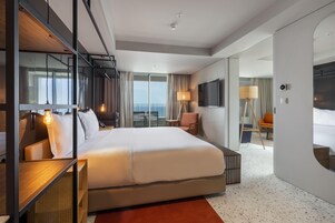 A modern hotel room with a large bed, a desk, a chair, a TV, and a view of the outdoors.