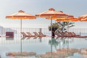 A poolside area with striped umbrellas, lounge chairs, and a view of the sea.