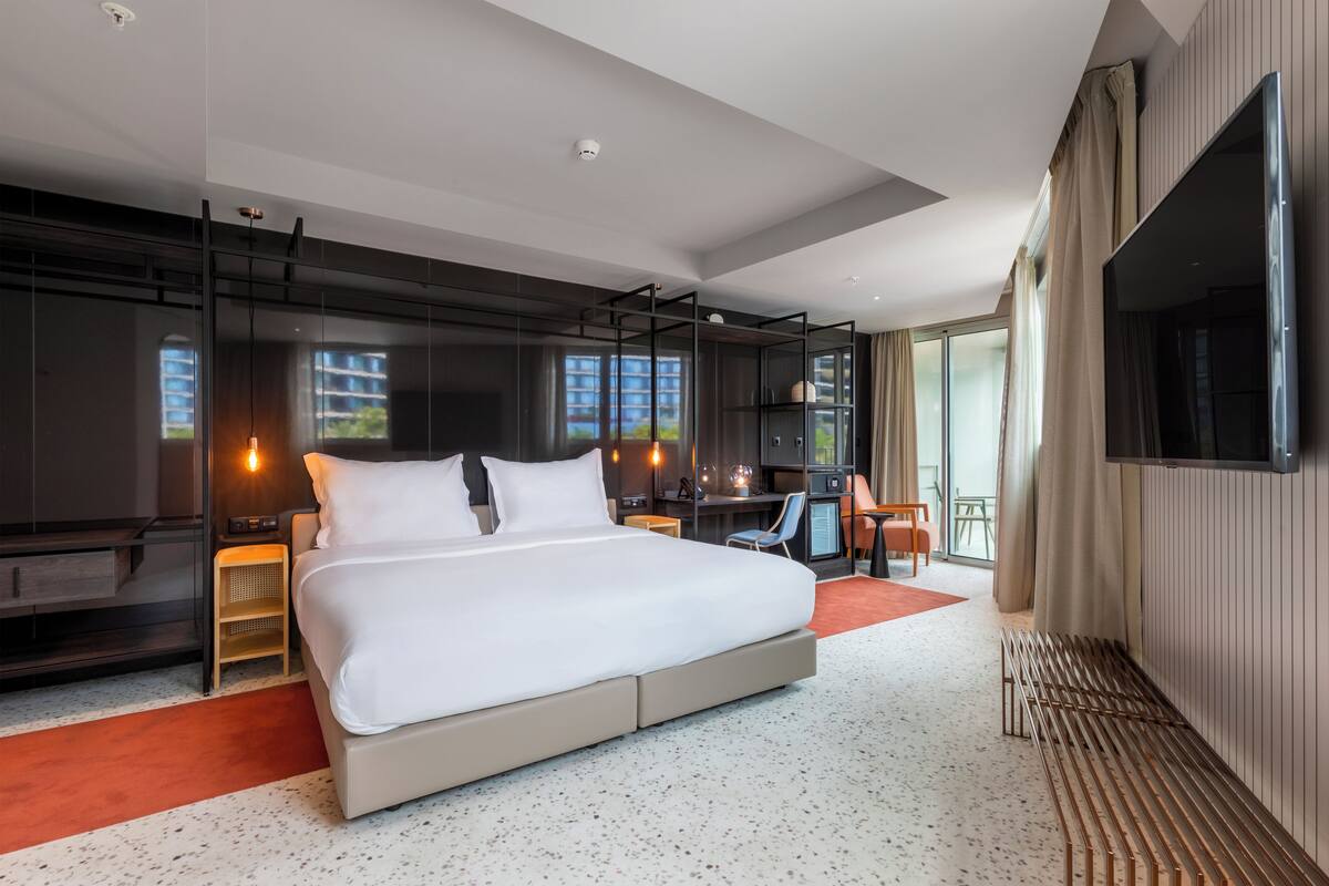Una habitación de hotel moderna con una cama grande, un escritorio, un televisor y un balcón con vistas a la ciudad.