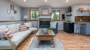A living room with a sofa, a coffee table, a fireplace, and a kitchen area with shelves and a countertop. - Downstairs Half of Home 3 bedrooms 1.5 bath 6 beds (Hudsonville)