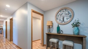 A hallway with wooden flooring, a wooden bench with two stools, a wall-mounted lamp, and a decorative tree artwork. - Downstairs Half of Home 3 bedrooms 1.5 bath 6 beds (Hudsonville)