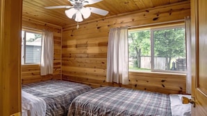 Eine Hütte mit zwei Betten, einem Deckenventilator und einem Fenster mit Vorhängen.