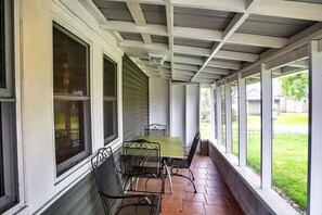 A covered porch with a table and chairs, large windows, and a view of a grassy yard.