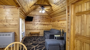 Ein rustikales Blockhaus-Interieur mit Deckenventilator, einer Couch, einem kleinen Tisch und einem an der Wand montierten Fernseher.
