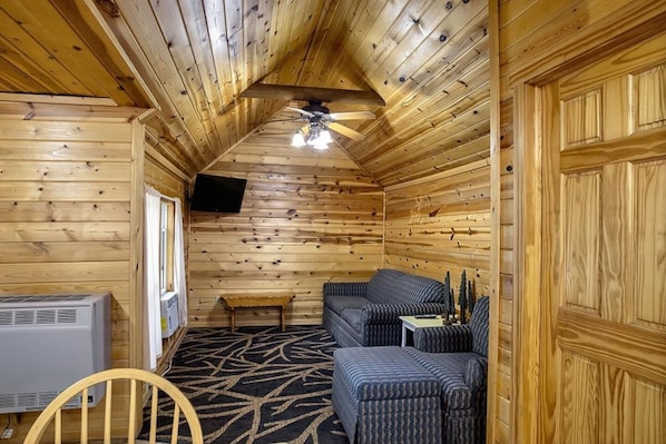 A log cabin interior with a ceiling fan, a sofa, a small table, and a television mounted on the wall.
