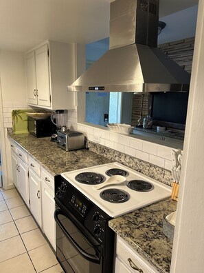 Enjoy cooking in this well-equipped kitchen with a stainless steel range hood, oven, and granite countertop.