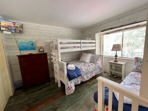 A bedroom with a bunk bed, a dresser, a small table, and a window with blinds.