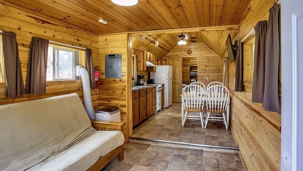 A wooden cabin interior with a sofa, dining table, chairs, kitchen area, and a ceiling fan. - Turtle Cabin Near Mississippi River (Buffalo City)
