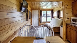 A wooden cabin interior with a television, a sofa, a table with a remote control, and a microwave. - Turtle Cabin Near Mississippi River (Buffalo City)
