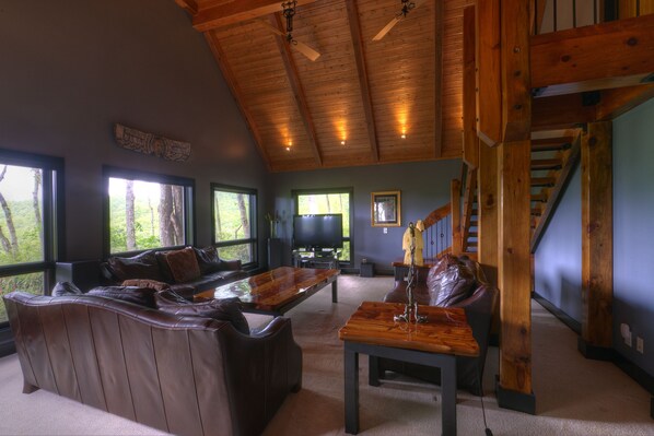 A spacious living room with a large wooden ceiling, a leather sofa, a wooden coffee table, and a television in the background.