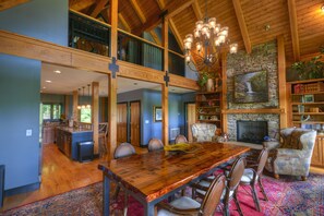 A spacious dining area with a large wooden table and chairs, a chandelier, and a fireplace.