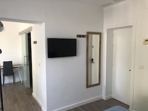 A modern room with a flat-screen TV mounted on the wall, a wooden-framed mirror, and a white door.