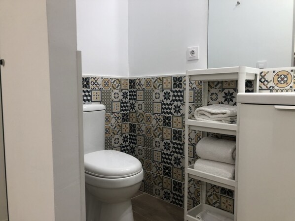 Une salle de bain avec des toilettes, une étagère avec des serviettes et un mur recouvert de carreaux à motifs.