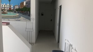 Un pasillo estrecho con un banco blanco, una puerta y un mural de una escena callejera.