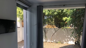 Una habitación con una puerta corrediza de vidrio que da a un jardín con árboles y una pared blanca.