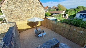 Een terras buiten met stenen muren, een tafel en stoelen, een witte parasol en een houten schutting.