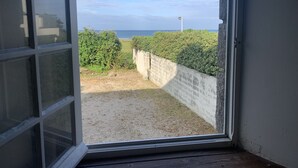 Een open deur die uitkomt op uitzicht over een strand, een haag en een heldere lucht.