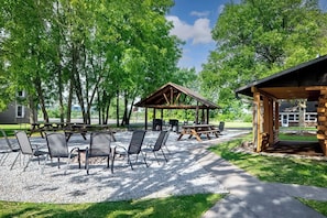 Een terras buiten met picknicktafels en stoelen, omringd door bomen.