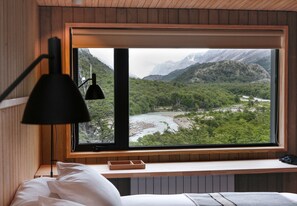 Une chambre dotée d’une grande fenêtre donnant sur une rivière et des montagnes.