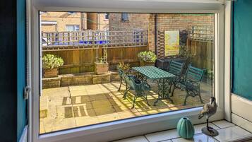 A view through a window of a patio area with a wooden fence, a table, and a bench.