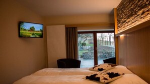Ein Schlafzimmer mit Bett, Fernseher an der Wand und Blick auf Garten und Steinmauer.