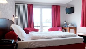 Ein Hotelzimmer mit Bett, Schreibtisch, Stuhl, Fernseher und einem Fenster mit Vorhängen.