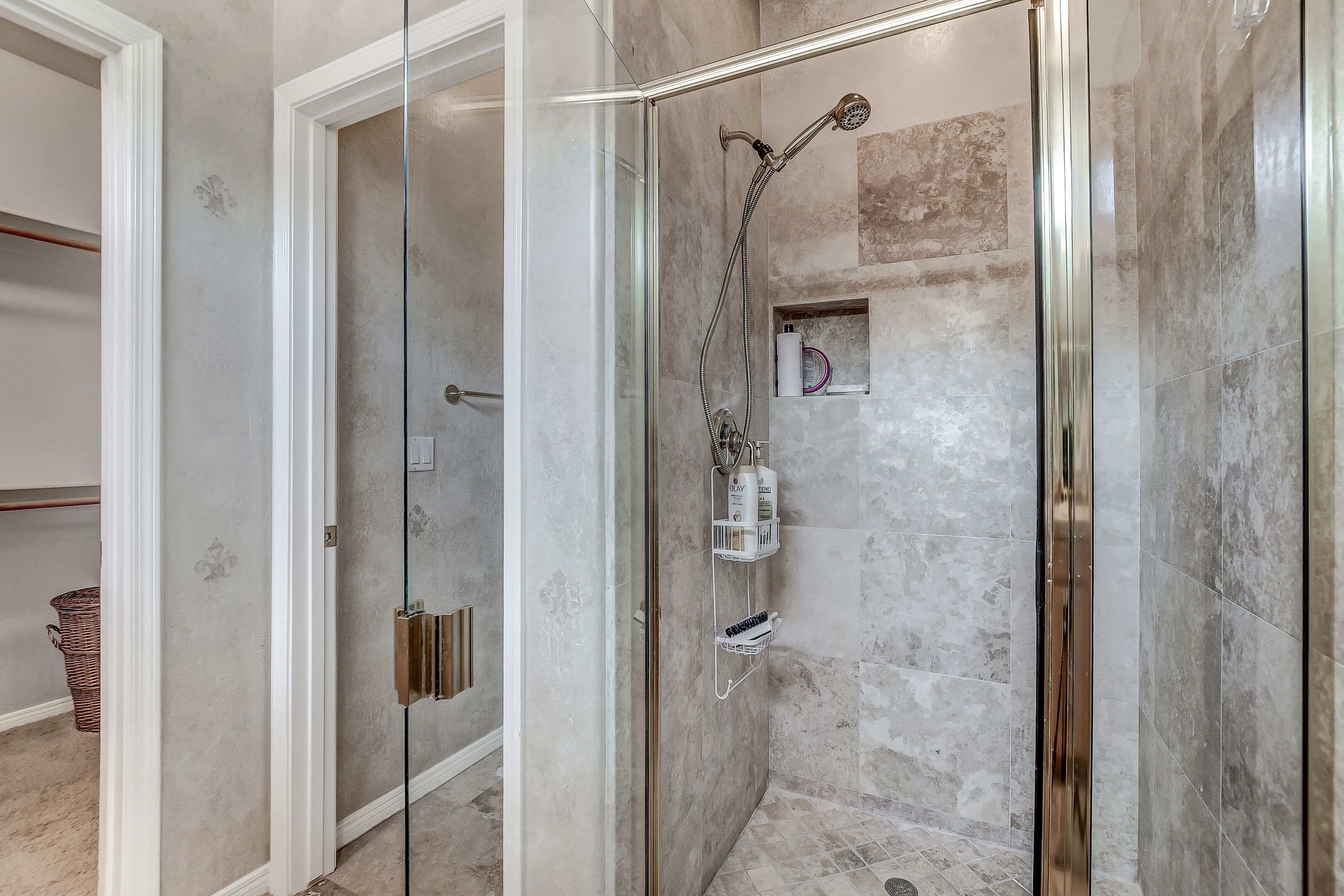 Eine gläserne Duschkabine mit Handbrause, ein integriertes Ablagefach für Toilettenartikel und eine Wand mit Marmorfliesen.