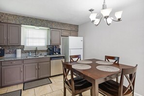 A compact kitchen with granite countertops, a refrigerator, and a dining area with four chairs and placemats.