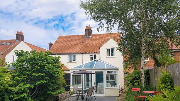 A house with a conservatory, a garden with a paved path, and a red fence. - 3 bedroom accommodation in Sheringham (Sheringham)