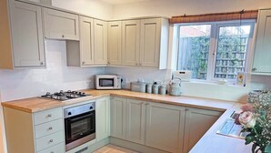 A kitchen with a gas stove, oven, microwave, and a window with a view of the outside. - 3 bedroom accommodation in Sheringham (Sheringham)