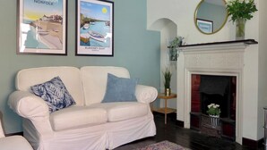 A living room with a white sofa, two framed pictures, a fireplace, and a mirror. - 3 bedroom accommodation in Sheringham (Sheringham)