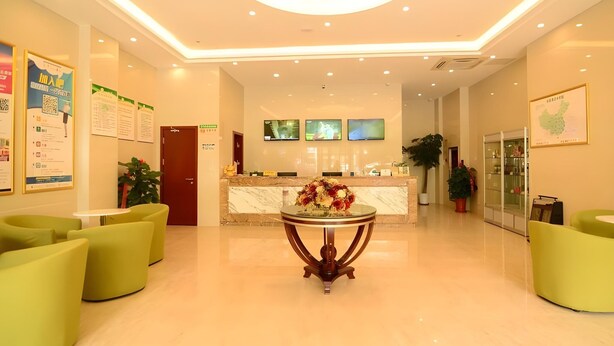 A hotel lobby with a reception desk, green seating, a central table with flowers, and a modern ceiling design. - Greentree Inn Suzhou Kunshan Huaqiao Metro Station Express Hotel (Suzhou)