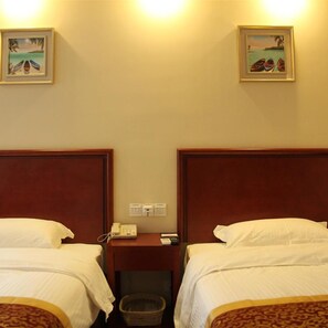 Une chambre d’hôtel avec deux lits, une table de chevet avec un téléphone et deux tableaux encadrés au mur.