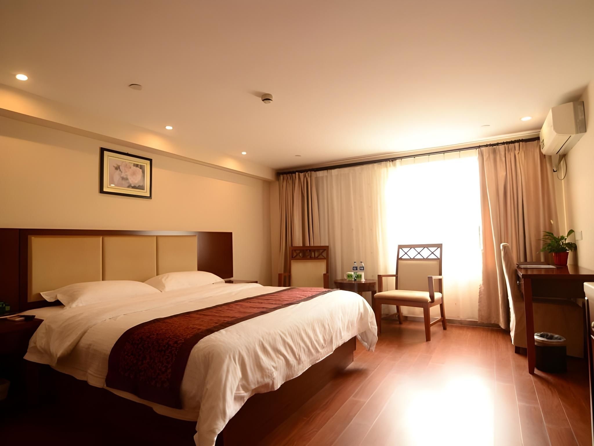 A hotel room with a large bed, a desk, a chair, and a window with curtains.