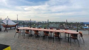 A rooftop terrace with a long table and chairs, a hanging chair, and a view of the cityscape. - Sonaview Hotel (Dumai)