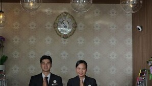 A reception area with a reception desk labeled "RECEPTIONIST" and two staff members standing behind it. - Sonaview Hotel (Dumai)