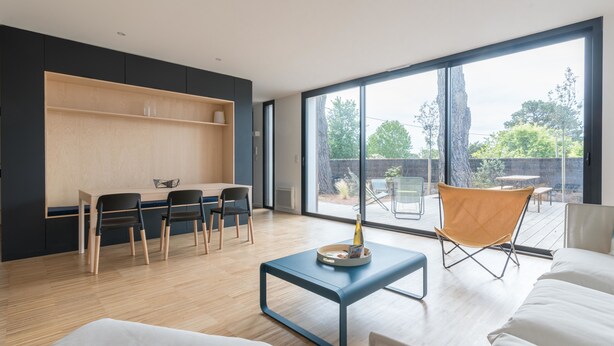 Una sala moderna con suelo de madera, un sofá, una mesa de centro y una zona de comedor con sillas.